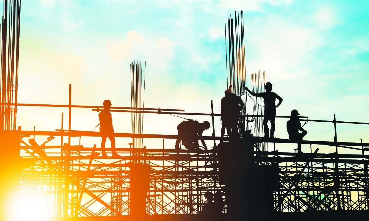 Construction crew erecting steelwork against a sunset sky