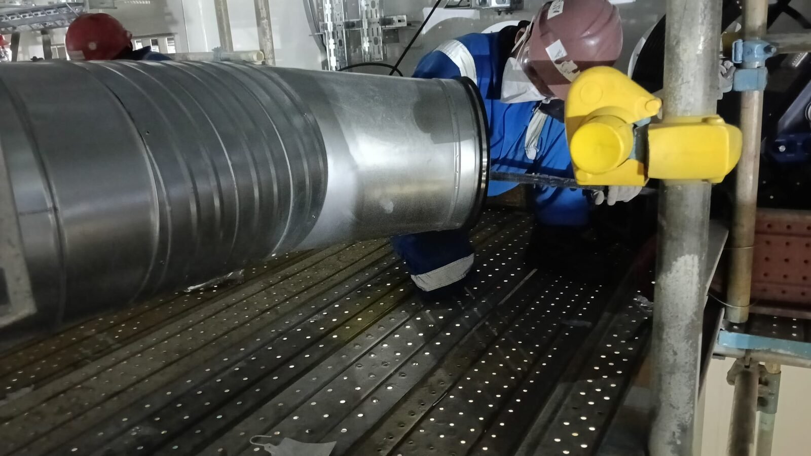 Crew fitting a coupling clamp to a spiral duct joint from scaffold