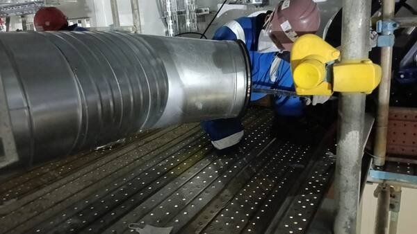 Crew fitting a coupling clamp to a spiral duct joint from scaffold